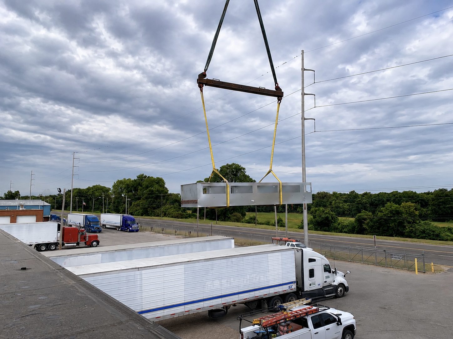 Crane lifting metal modular unit over trailers